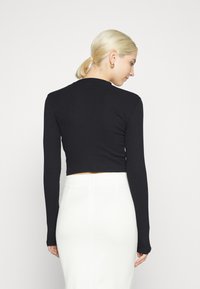 Top cropped preto de manga longa com um design ajustado, textura canelada e um decote redondo, usado com uma saia branca.