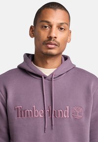 Felpa in cotone viola con ricamo del testo e logo "Timberland". Cappuccio regolabile con coulisse e texture morbida.