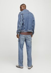 Jeanjakke med klassisk pasform, lyseblå farve og synlige syninger, parret med løstsiddende blå jeans og grå sandaler.