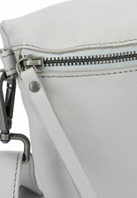 Borsa in pelle grigia chiara con chiusura a zip con denti metallici a contrasto, tracolla piatta e dettagli di cucitura visibili.