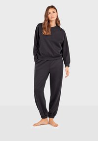 Conjunto de sudadera y pantalones a juego de algodón negro. Cuenta con puños elásticos en las mangas y los tobillos, corte relajado y textura suave.