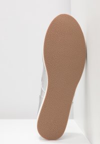 Baskets argentées avec une semelle en caoutchouc texturée, dotées d'un dessus lisse et d'accents latéraux dans une teinte contrastante.