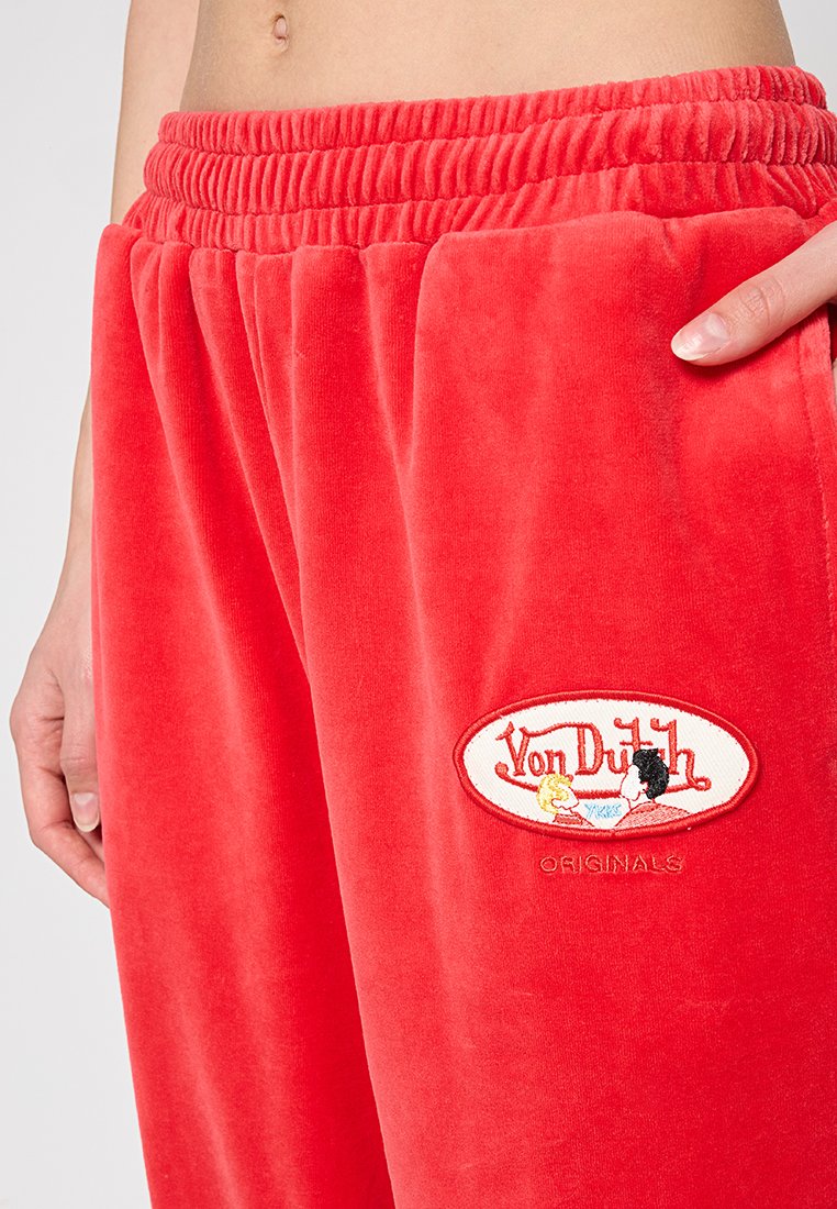 Rote Velours-Sweatpants mit elastischem Bund und gesticktem Logopatch mit Cartoonfiguren und Text. Weicher Stoff, lockere Passform.