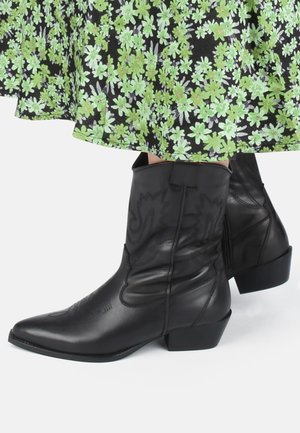 Botas de vaquero de cuero negro con punteras puntiagudas, tacones cuadrados y costuras decorativas. Suave textura con cierre de cremallera en el lateral.