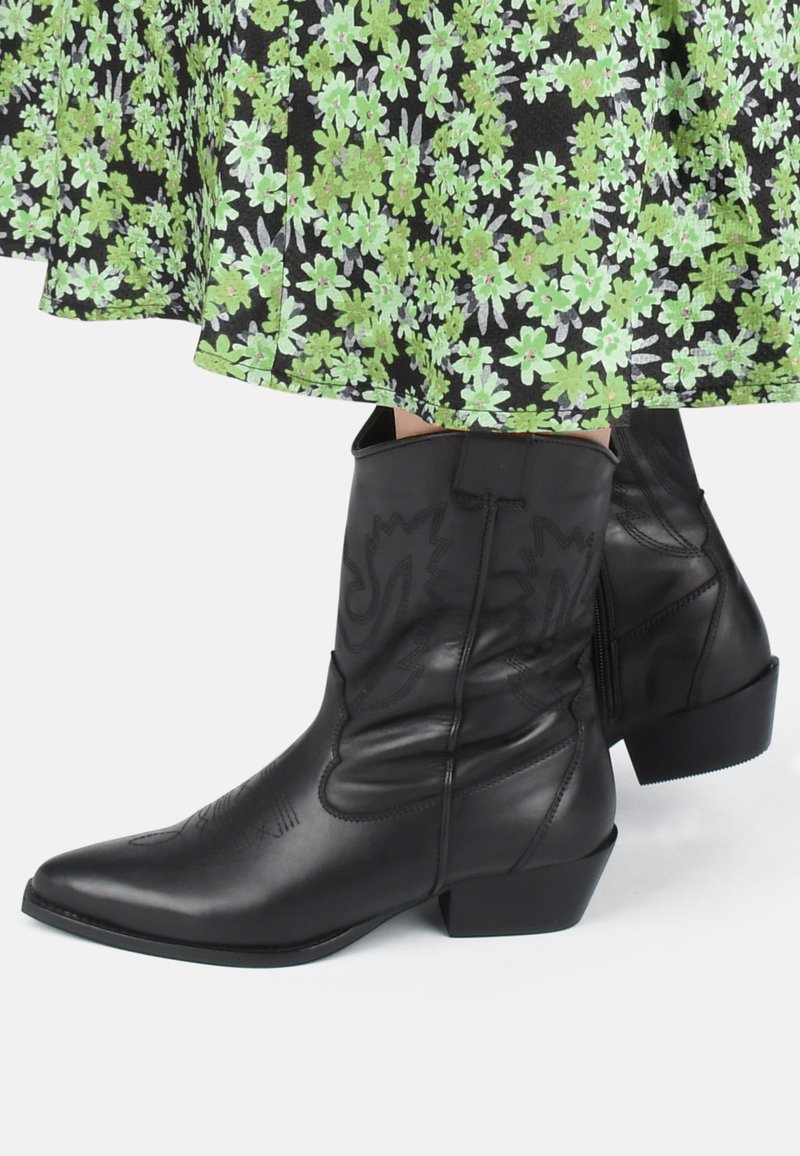 Botas de vaquero de cuero negro con punteras puntiagudas, tacones cuadrados y costuras decorativas. Suave textura con cierre de cremallera en el lateral.