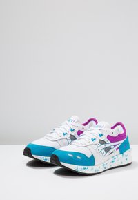 White athletic shoes with turquoise and purple accents, mesh panels, black detailing, and a patterned sole for grip.