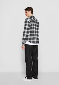Sort og hvidt ternet flannel skjorte med afslappet pasform, lange ærmer og sideslidser, parret med mørke bukser og hvide sneakers.