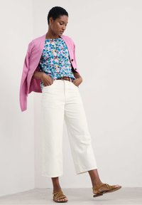 Pink knit cardigan, floral print top with blue, green, and pink hues, white wide-leg pants, and brown strappy sandals.