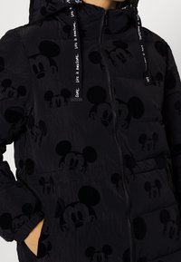 Chaqueta acolchada negra con un diseño de acolchado que presenta motivos en relieve de Mickey Mouse. Cierre de cremallera, capucha ajustable y cordones de marca.