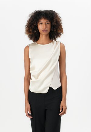 Sleeveless, cream-colored satin top with a draped front detail and rounded neckline, paired with black pinstriped pants.