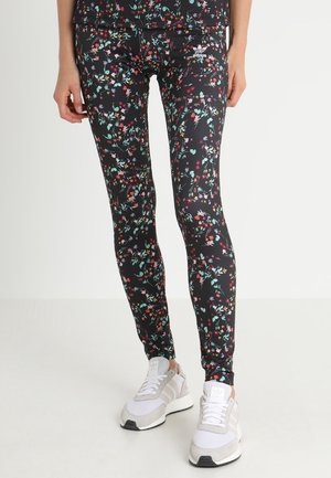 Leggings neri con un motivo floreale che presenta fiori rossi, blu e verdi; realizzati in un materiale elastico; abbinati a sneakers bianche e grigie.