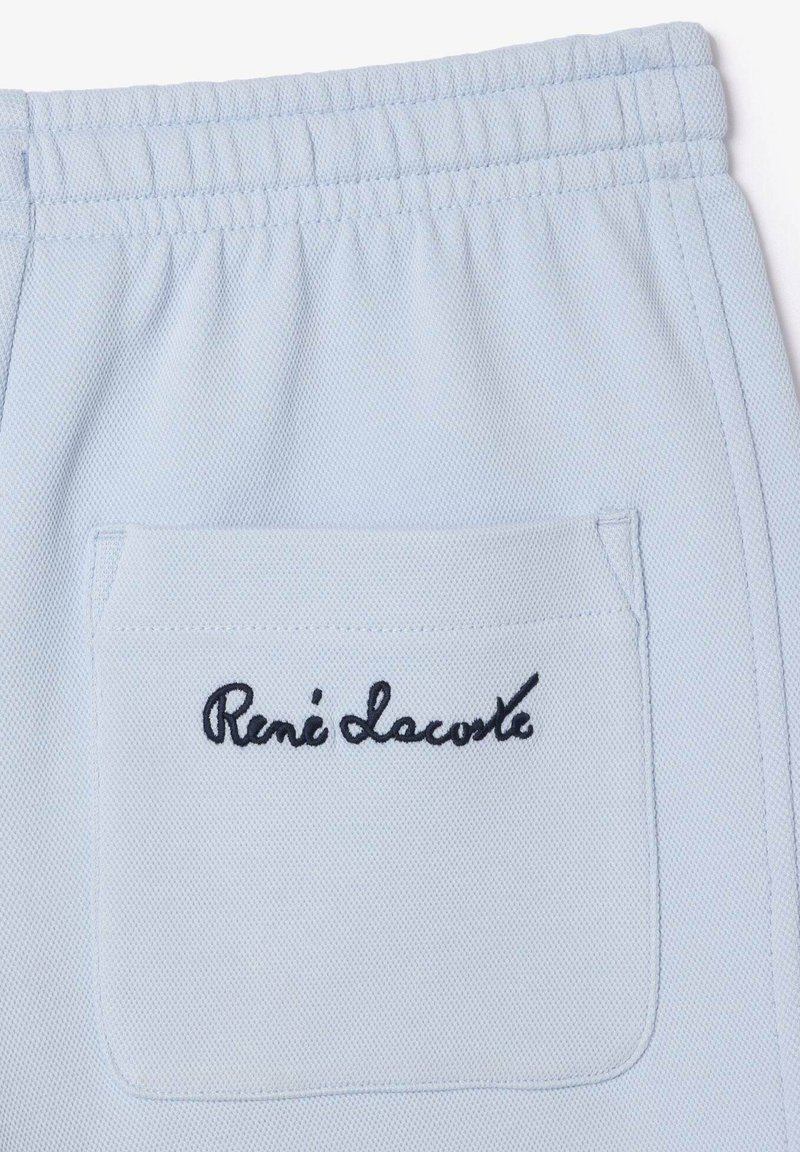 Shorts de algodón azul claro con cinturilla elástica, que cuentan con un bolsillo trasero decorado con el texto bordado en negro "René Lacoste".