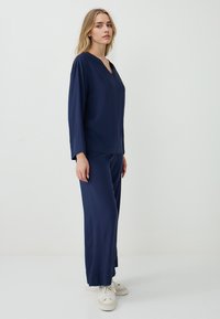 Navy blauwe loungewear set van zachte stof, met een V-hals top en wijde broek, voorzien van een borstzak en een flowy ontwerp.