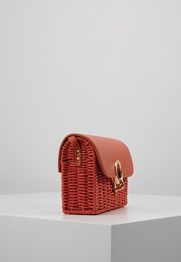 Rode geweven handtas met een gebogen leren klep en gouden hardware. Vierkante vorm met een getextureerde afwerking en een opvallend zijgespsdetail.