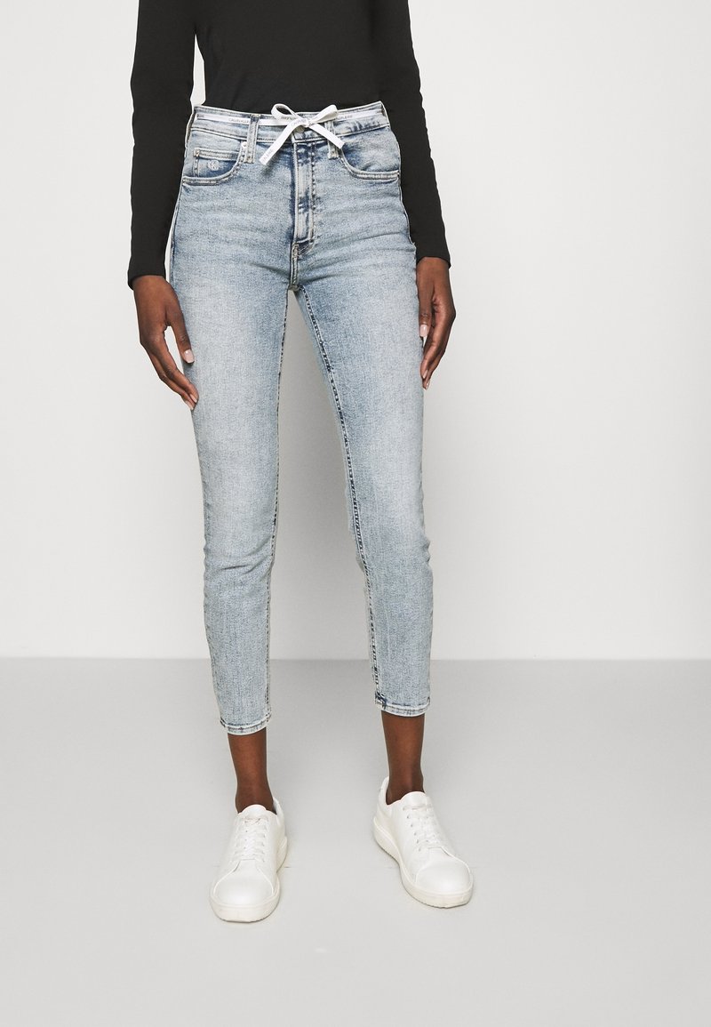 Ljust blå denimjeans med smal passform och avkortad längd. Har en vit dragsko i midjan och uppvikta fållar. Matchas med vita sneakers.