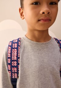 Gray sweatshirt with ribbed collar and blue backpack straps featuring a repeated red "GO! SPIDEY!" text pattern, against a neutral background.