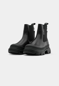 Botas de tornozelo pretas apresentam um upper em couro liso, painéis laterais elásticos e uma sola de borracha chunky com um padrão de ranhura texturizado.