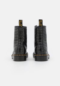 Svarta ankelstövlar i strukturerad syntetläder med krokodilmönster. Har gula detaljer och en kraftig, hållbar sula.