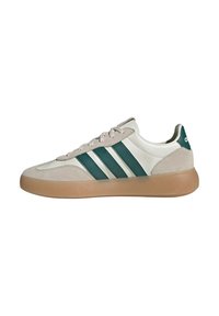 Sneaker Adidas beige e bianco con tre strisce verdi, punta e tallone in suede e suola in gomma caramello, vista laterale su sfondo bianco.