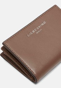 Bruine leren portemonnee met een gladde textuur, gestikte randen en het ingegraveerde logo "LIEBESKIND BERLIN" aan de voorkant. Compact, met een bi-fold ontwerp.