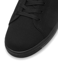 Melns sporta apavu ar teksturētu auduma augšējo daļu, apaļu purngalu, sešas acis ar kurpju šņorēm un melnu gumijas zoli ar horizontālām rieviņām.