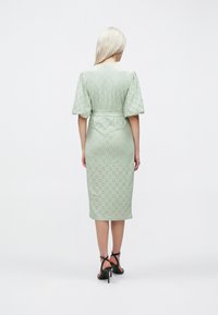 Lys grøn kjole til knærne med korte puffærmer, med hullmønster og belte i taljen, båret med stroppede sorte hæle.