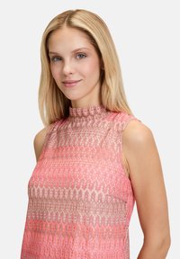 Rosa und beige ärmelloses Oberteil mit hohem Kragen, das über ein strukturiertes Muster und subtilen Glanz verfügt.