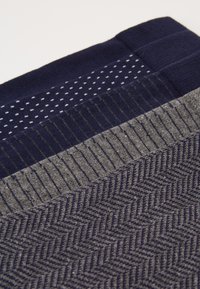 Marineblaue und graue gemusterte Socken zeigen Fischgrätenmuster, Streifen und Punkte in unterschiedlichen Texturen, die in horizontalen Reihen angeordnet sind.