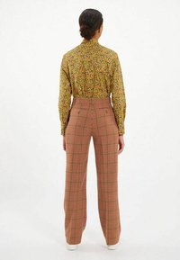 Chemise à manches longues jaune avec imprimé floral, associée à un pantalon large taille haute à carreaux rouges et beiges. Baskets blanches.