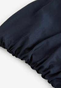 Tummansininen kangas, jossa on sileä pinta ja rypytetty elastinen yksityiskohta reunassa, mikä luo pehmeän ja istuvan ilmeen.