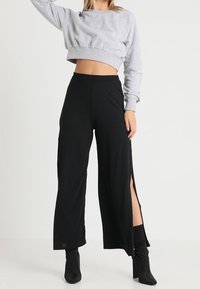 Felpa grigia corta con texture a coste, abbinata a pantaloni neri a gamba larga con righe sottili e spacchi laterali. Outfit completato da stivaletti neri alla caviglia.