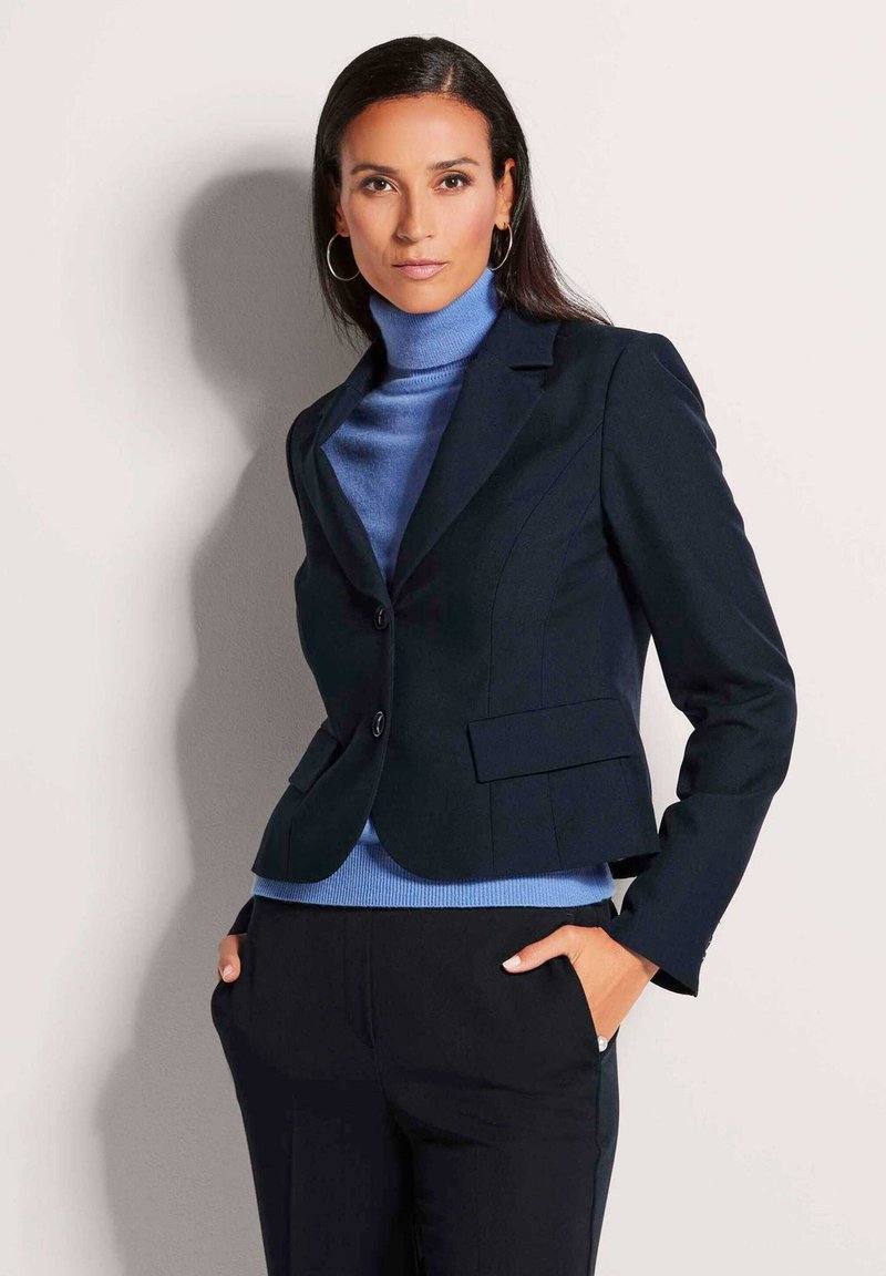 Marineblazer met twee knopen en zijzakken, gecombineerd met een lichtblauwe coltrui. Glad materiaal met een aangesloten ontwerp.