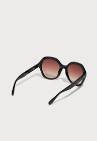 Schwarze achteckige Sonnenbrille mit verlaufenden braunen Gläsern. Eleganter Kunststoffrahmen mit glatter Oberfläche und gebogenen Bügeln. Sichtbares goldenes Logo-Detail.