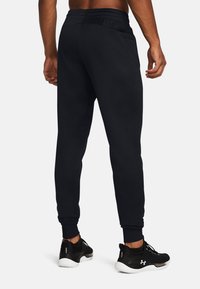 Sorte joggingbukser med elastisk talje, sidelommer og ribbede manchetter. Stoffet ser glat ud med en afslappet pasform, kombineret med sorte sneakers.