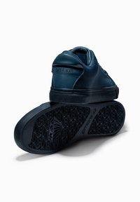 Tmavě modré tenisky s hladkým syntetickým svrchním materiálem a texturovanou gumovou podrážkou, se geometrickým vzorem a vyraženým logem na patě.