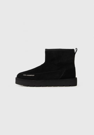 Black suede ankle boots with a rounded toe, flat rubber sole, stitched detailing, and rear pull tab. Karl Lagerfeld logo on the side.