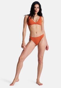 Ensemble bikini orange avec un motif texturé. Le haut a une forme triangulaire, et le bas est taille basse avec une couverture minimale.