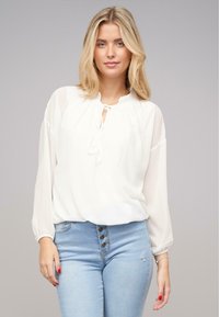 Hvid bluse med en rund halsudskæring og nøglehul detalje. Sukkersøde lange ærmer og teksturstof. Parret med lyseblå slidte jeans.