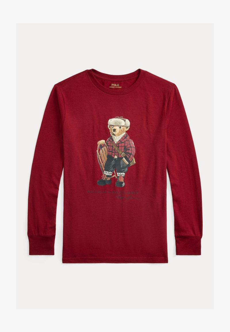 Piros hosszú ujjú póló, amin egy kockás inges, téli felszerelést viselő és szánkót tartó medve illusztrációja látható.