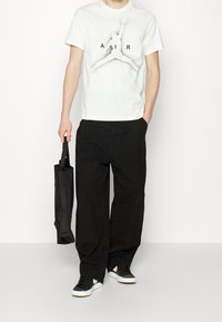 Vit bomulls t-shirt med en svart grafik av en hopparfigur och ordet "AIR." Matchad med lösa svarta byxor och svarta sneakers.