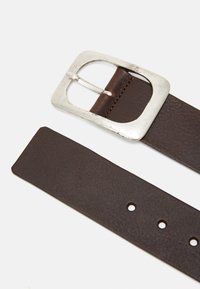 Ceinture en cuir marron avec une surface texturée, dotée d'une boucle rectangulaire en argent et de plusieurs trous de réglage le long de la sangle.