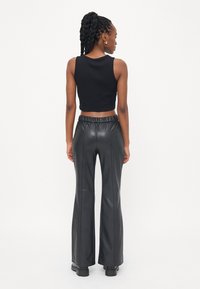 Zwarte cropped tanktop gecombineerd met hoge taille fluwelen flared pants van zwarte nepleer, met een elastische tailleband en een gladde textuur.