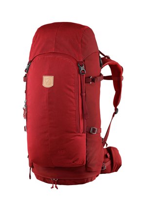 Red fabric backpack with a rounded top, adjustable straps, and multiple pockets. Features a leather logo patch and durable hardware.