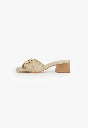Mule beige con punta aperta, tomaia in pizzo intrecciato, dettaglio fibbia dorata e tacco basso a blocco impilato su sfondo bianco.