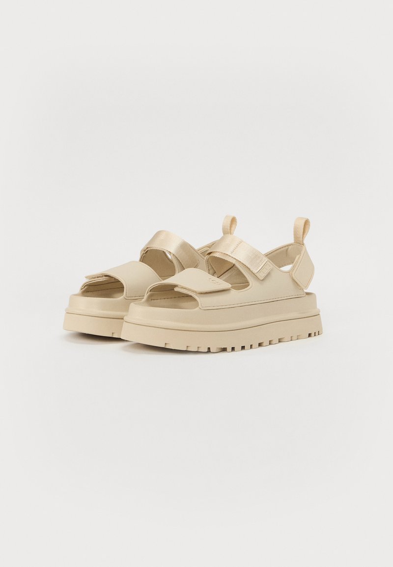 Beige Plattformsandalen mit offenem Zehenbereich, breiten Klettverschlussriemen und einer dicken strukturierten Sohle mit einem robusten Profilmuster.