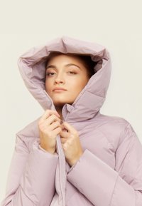 Light lavender puffer jacket with a high collar and oversized hood. Smooth texture, zip closure, and stitching details visible.