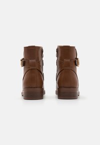 Bottines en cuir marron avec une finition lisse, un bout arrondi, des accents de double boucle, et un talon empilé avec de subtiles lignes horizontales.