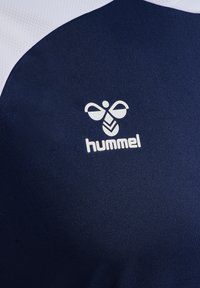 Granatowa sportowa koszulka z białym akcentem. Charakteryzuje się fakturowaną tkaniną oraz wyraźnym białym logo z motywem pszczoły.