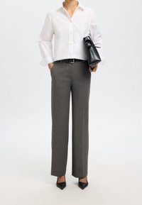Biała koszula z kołnierzykiem i podwiniętymi rękawami, szare dopasowane spodnie, czarny pasek oraz czarna stylowa torebka o eleganckim designie i szpiczastych obcasach.