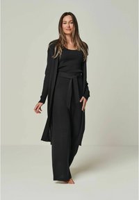 Schwarzes gestricktes Loungewear-Set mit einer langen Strickjacke, weit geschnittenen Hosen mit einem Bindegürtel und einem enganliegenden Oberteil. Weiche Textur und minimalistisches Design.